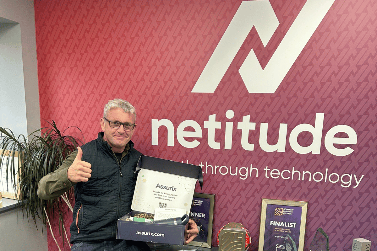 Netitude Managing Director, Adam Harling, holding Assurix welcome box in one hand and raising the other hand in celebration, marking MSP trust mark achievement