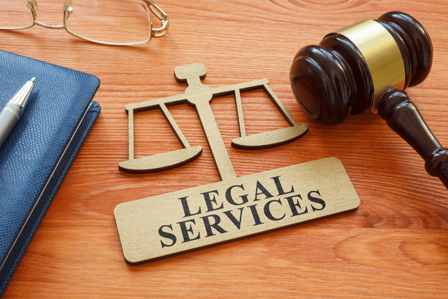 Legal services symbol on a table alongside a hammer, journal and a pair of glasses.