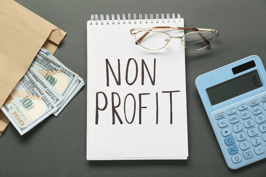 A notepad with the words non profit written across the front page with money, glasses and a calculator situated in the frame.