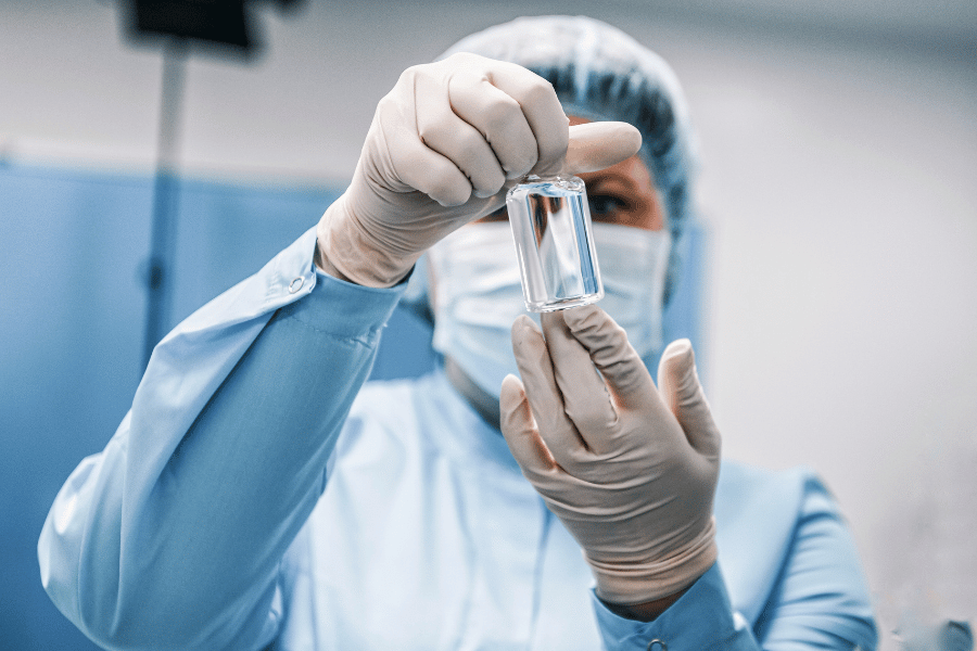 A pharmaceutical services professional holding a test tube whilst wearing full PPE.
