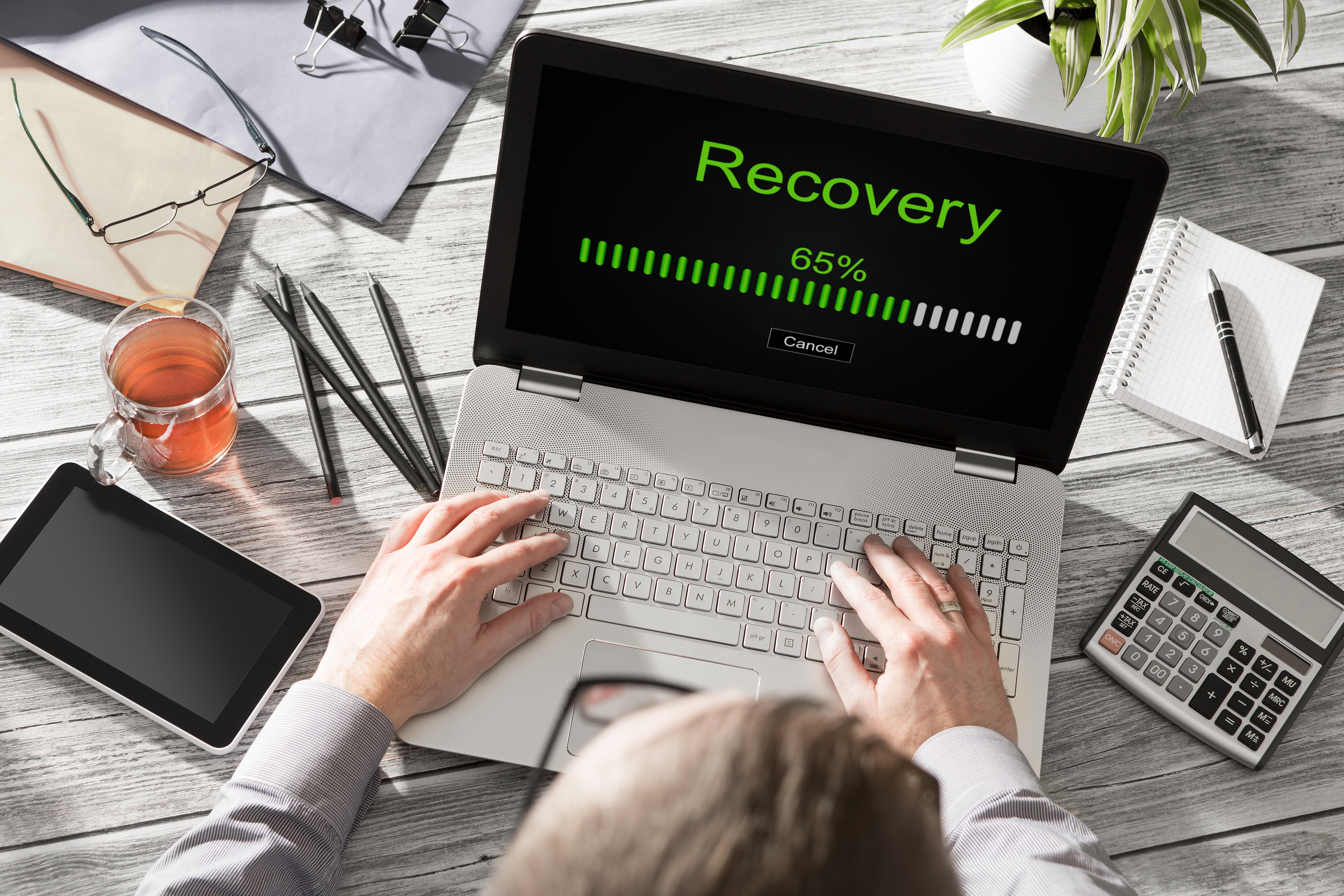 Image of person working on a laptop that has 'recovery' and a progress bar lit up in green, displayed on the screen.