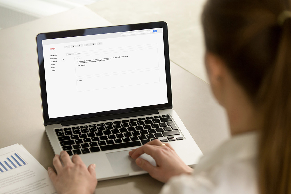 Businesswoman typing corporate e-mail using laptop at office desk.