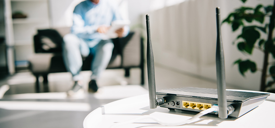 selective focus of black plugged router on white table and businessman sitting on sofa