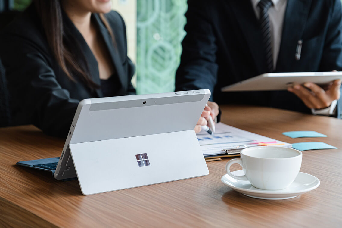 Microsoft Surface tablet on desk with businessman and businesswoman discussing background.