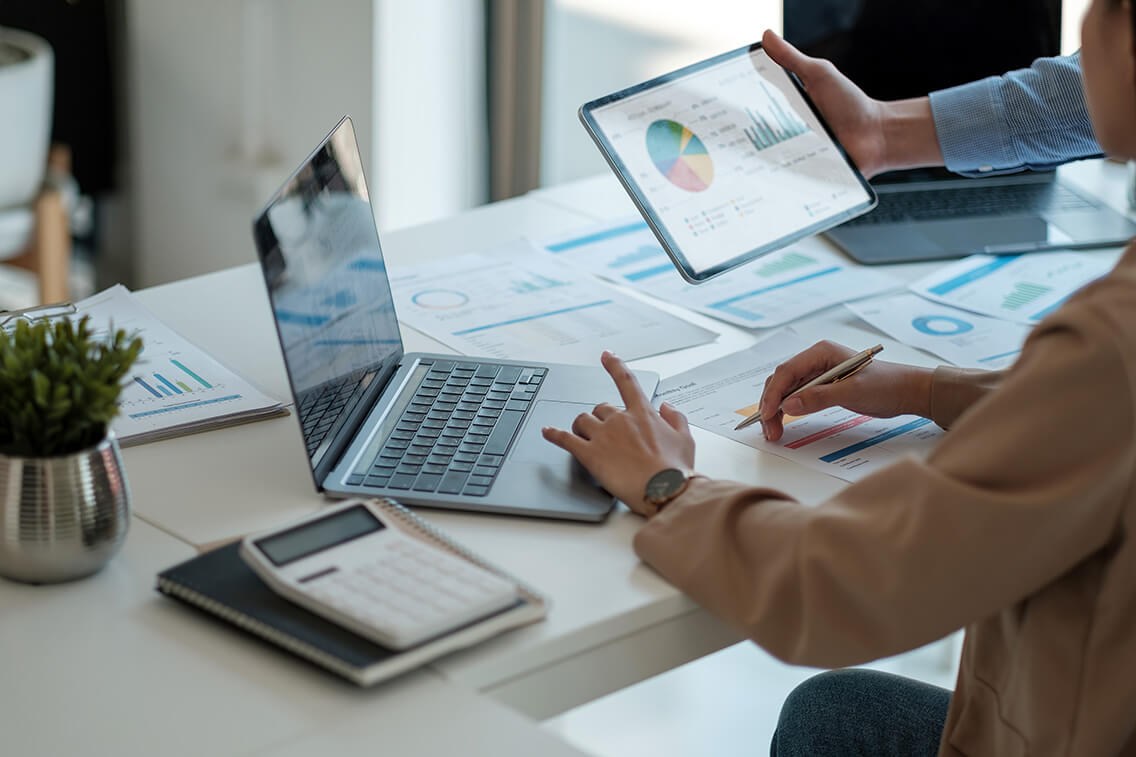 Two people looking data across a mixture of paper, laptops and tablets