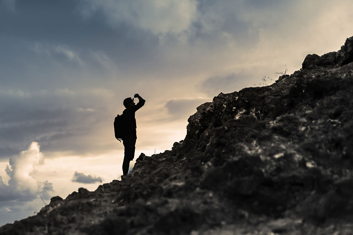 Man getting ready to climb up mountain looking up at the challenge before him. Believe in yourself, overcoming challenges, pushing forward concept.