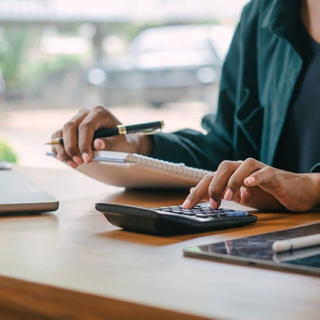 Person holding a piece of paper and pen, whilst pressing buttons on a calculator. 