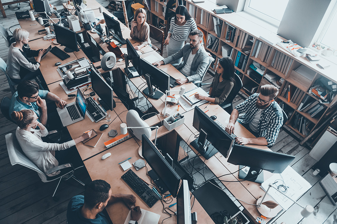 Confident business experts a work. Top view of group of young business people in smart casual wear working together while sitting at the large office desk