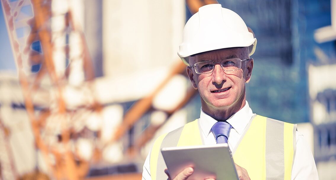 Senior engineer man in suit and helmet working on tablet pc