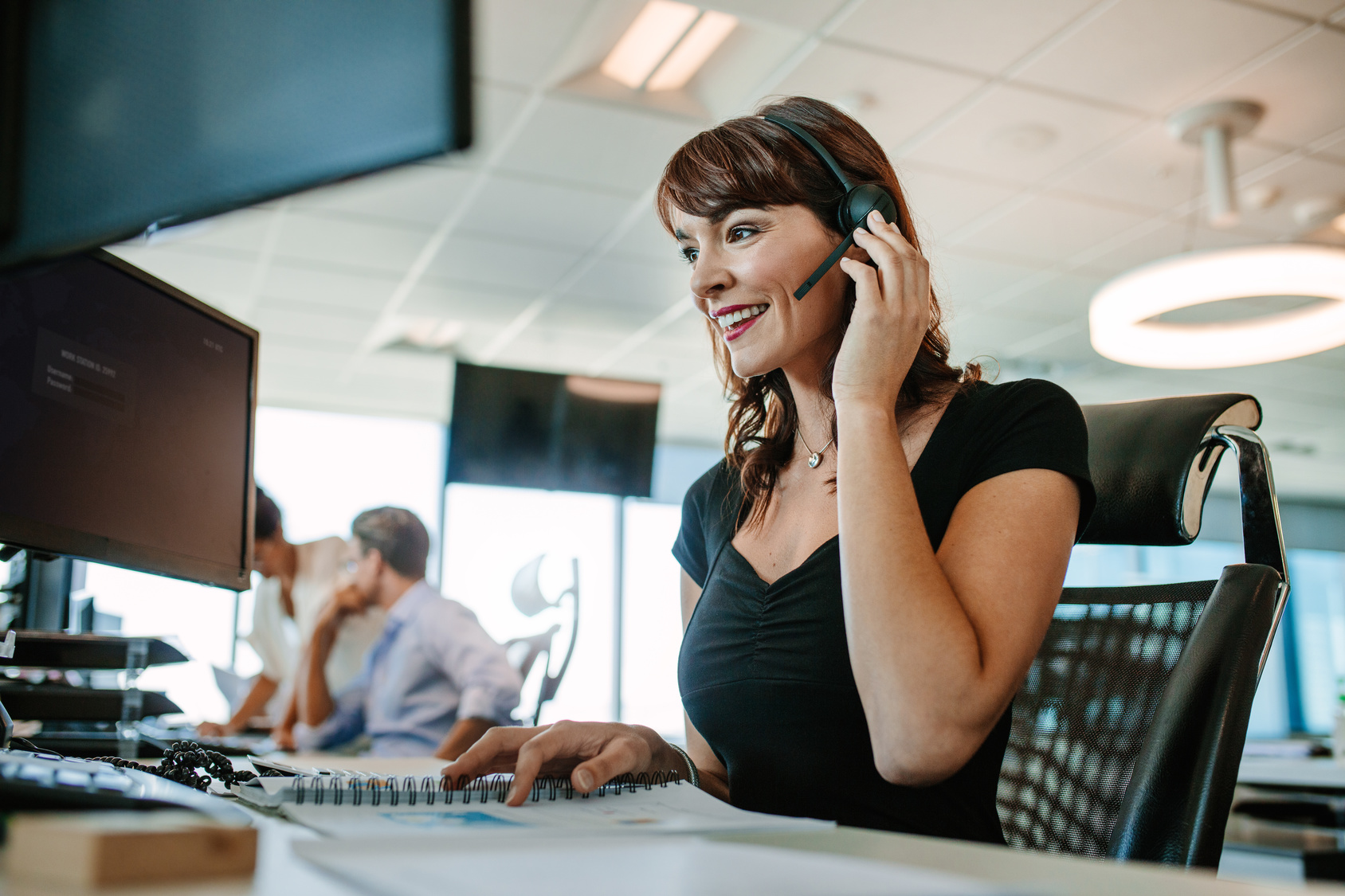 Image of woman smiling whilst talking to somebody through a headpiece. 