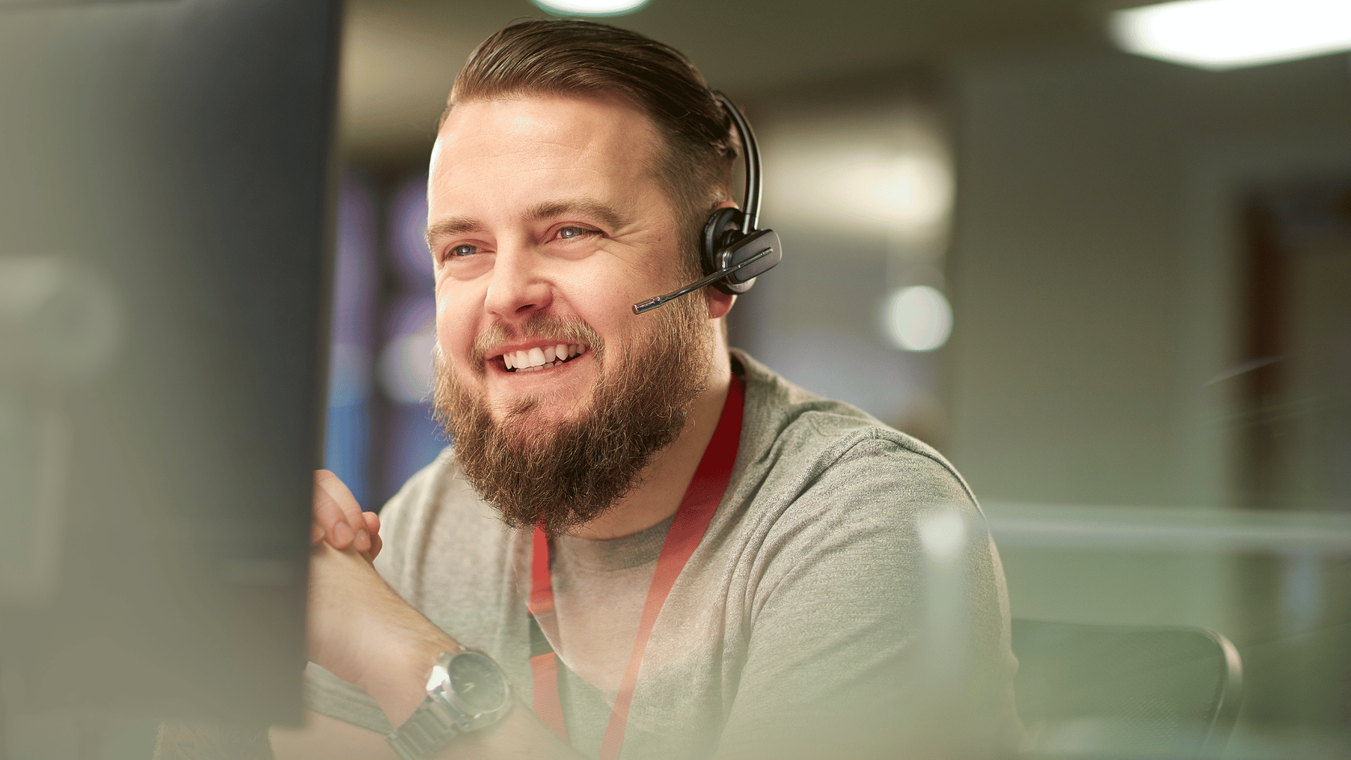 IT support professional wearing a headset working at a computer in a modern helpdesk environment.