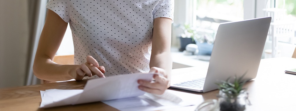 Young woman working from home, holding a piece of page and using a calculator