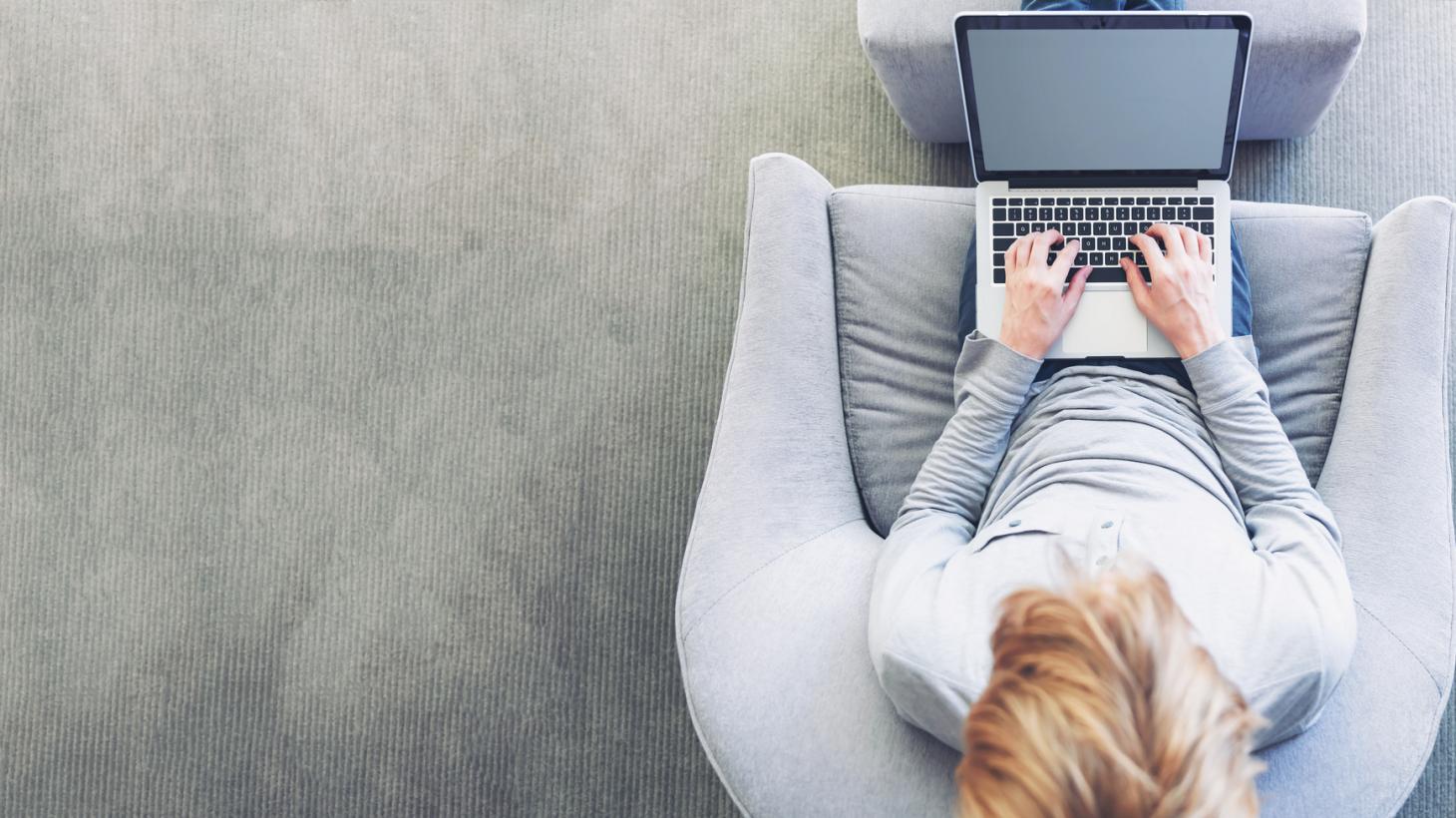 A person sat on an arm chair while using their laptop