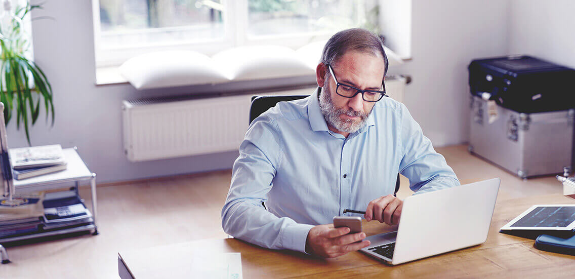 Grey Bearded mature man creative director sitting in modern office working with laptop computer on wooden desk. stylish design interior