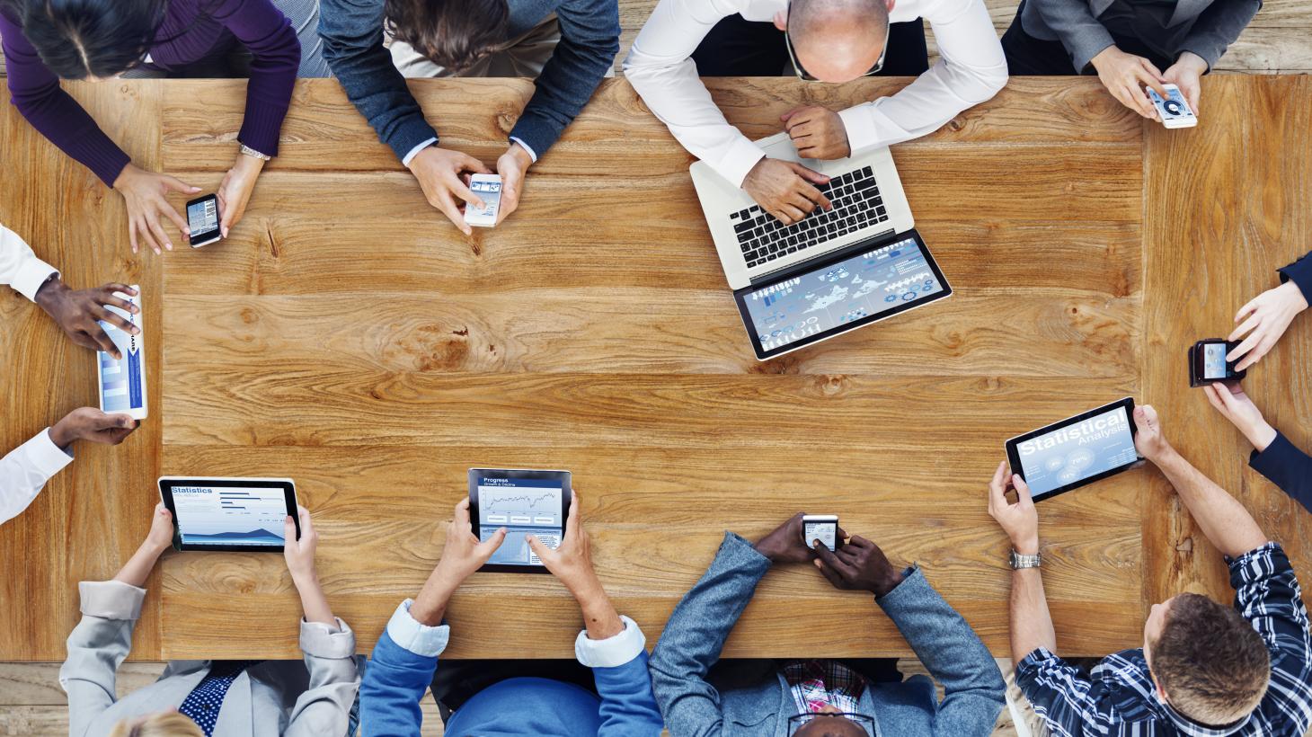 A group of people gathered around a table using different devices.