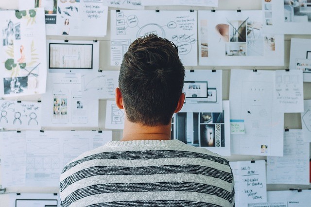 A man looking at a pinboard full of different sketches and notes