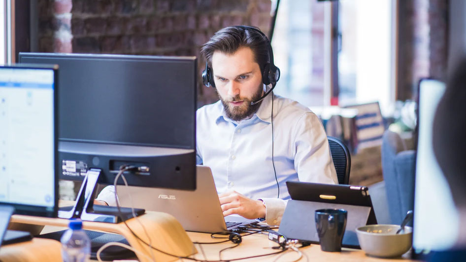 Young male customer service engineer working on a laptop at his desk