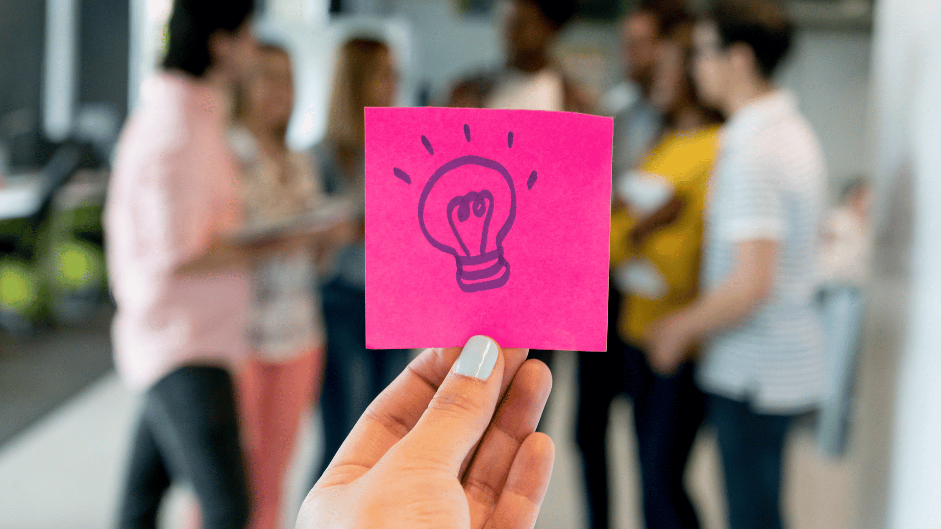Photo of a light bulb on a sticky note with people innovating in the background