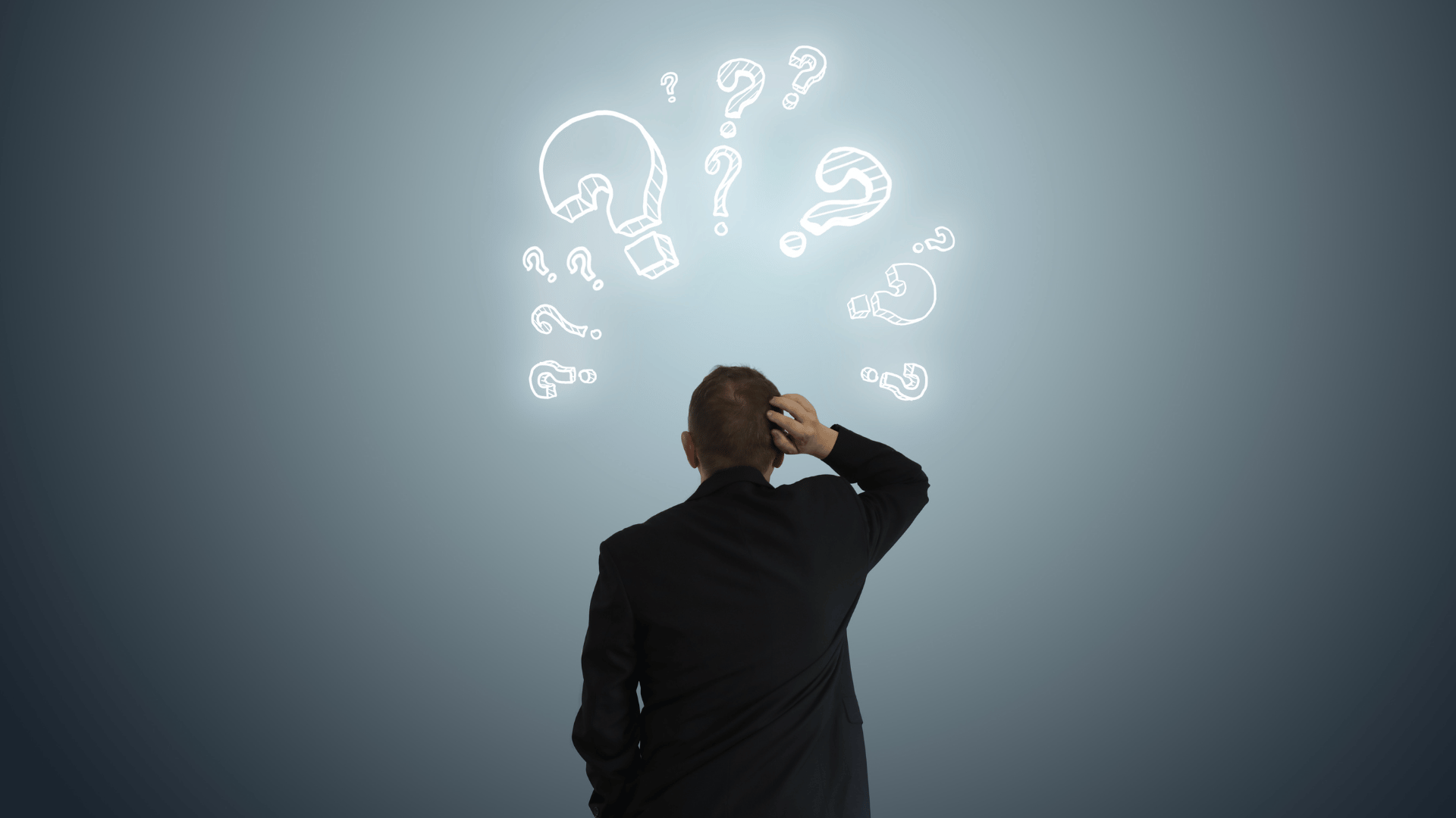 Man scratching his head looking away from the camera looking at illuminated question marks.
