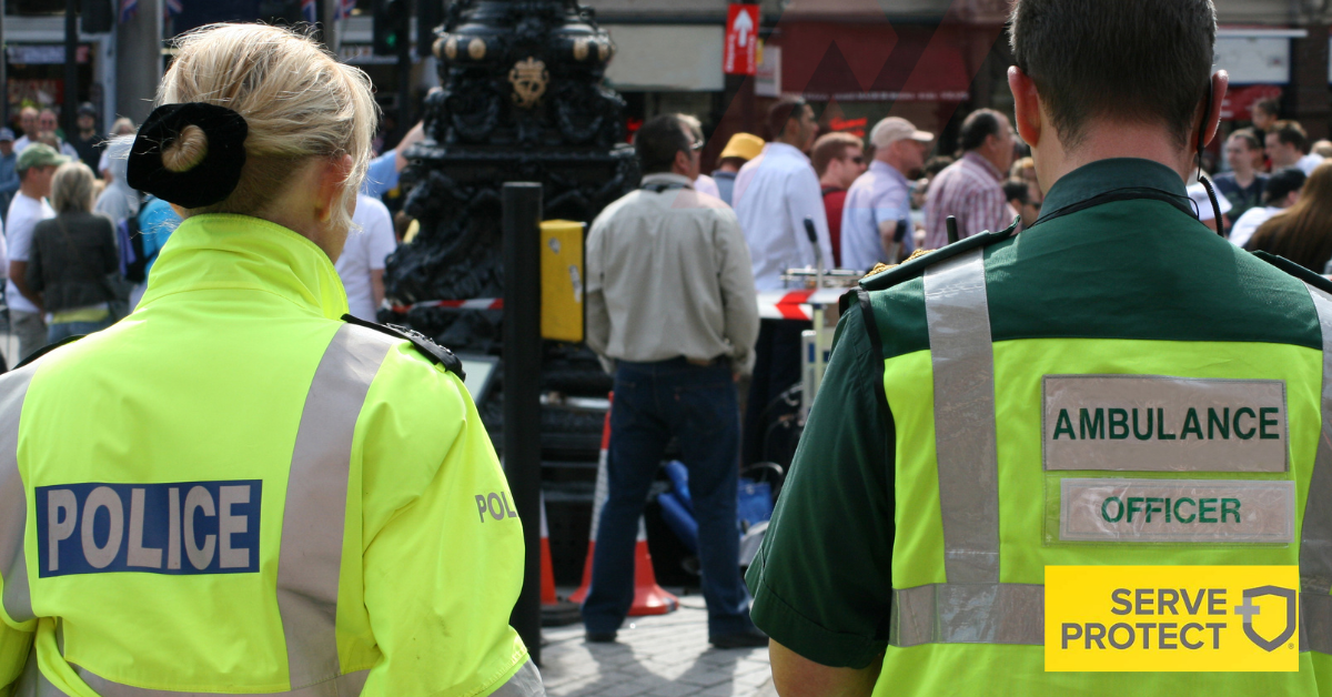 Wide angle shot of a police officer and ambulance officer working side-by-side with their backs to the camera.