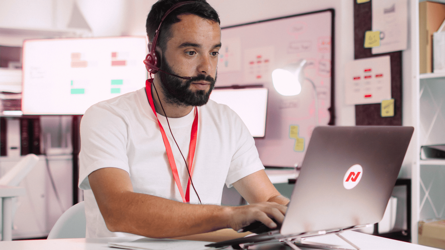 Person wearing a headset working on a laptop in a modern office environment, representing remote communication and telephony.