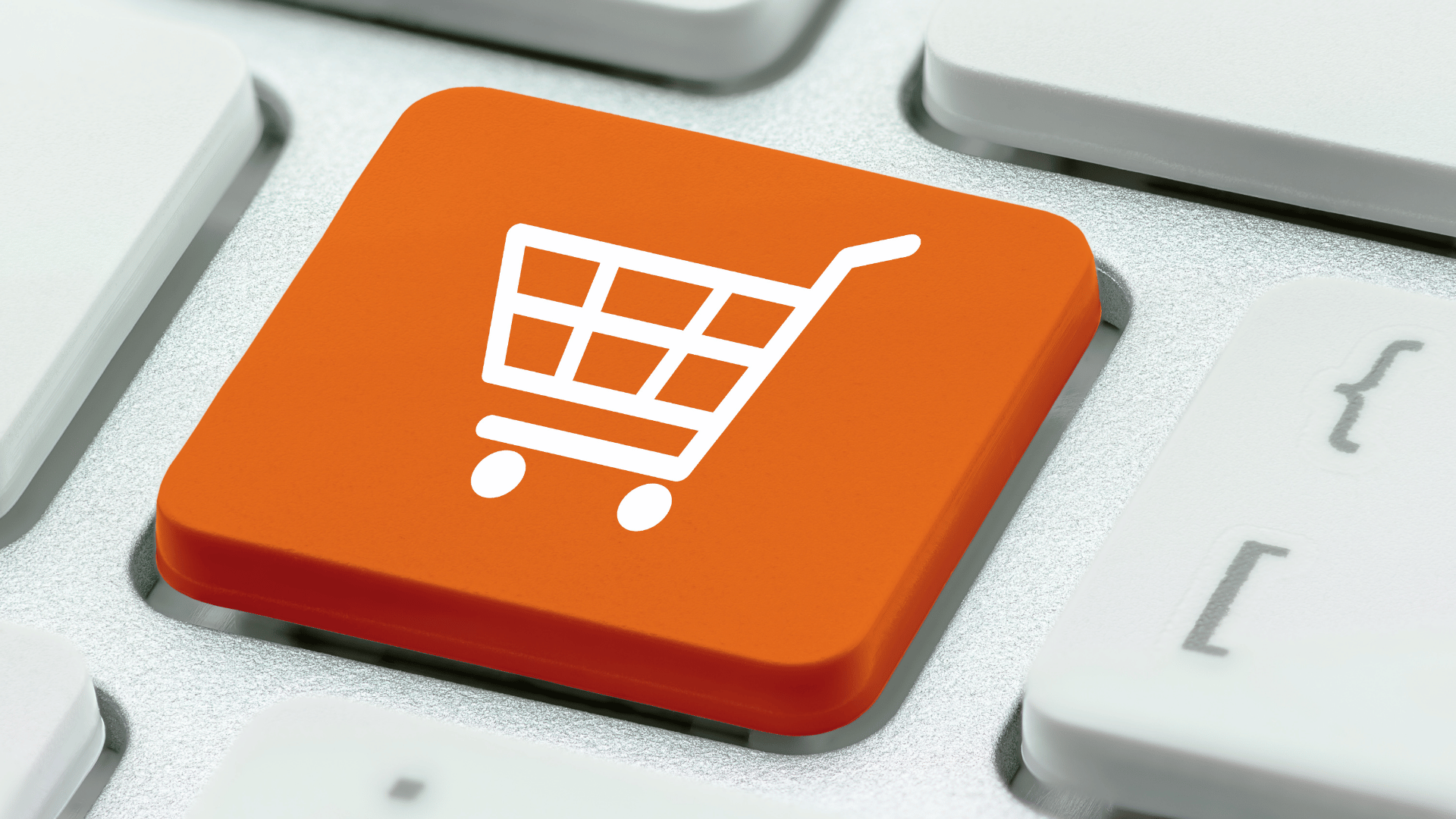 An icon of a shopping trolley on an orange button in a close up image of a keyboard.