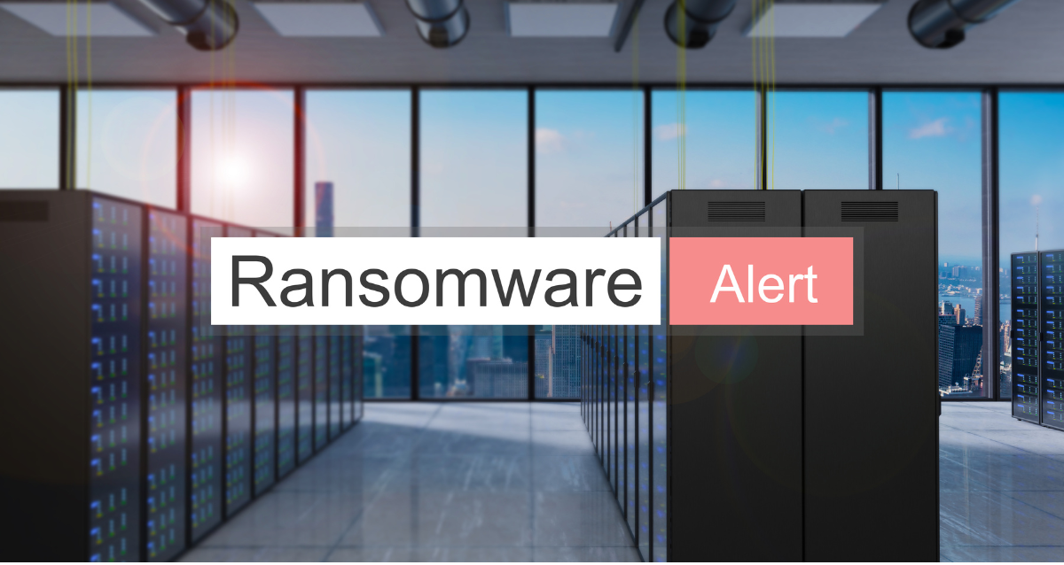 Photo of what appears to be an office building in a city with big, floor to ceiling windows. This image has the text Ransomware Alert displayed in the middle section with a white and red background respectively. 