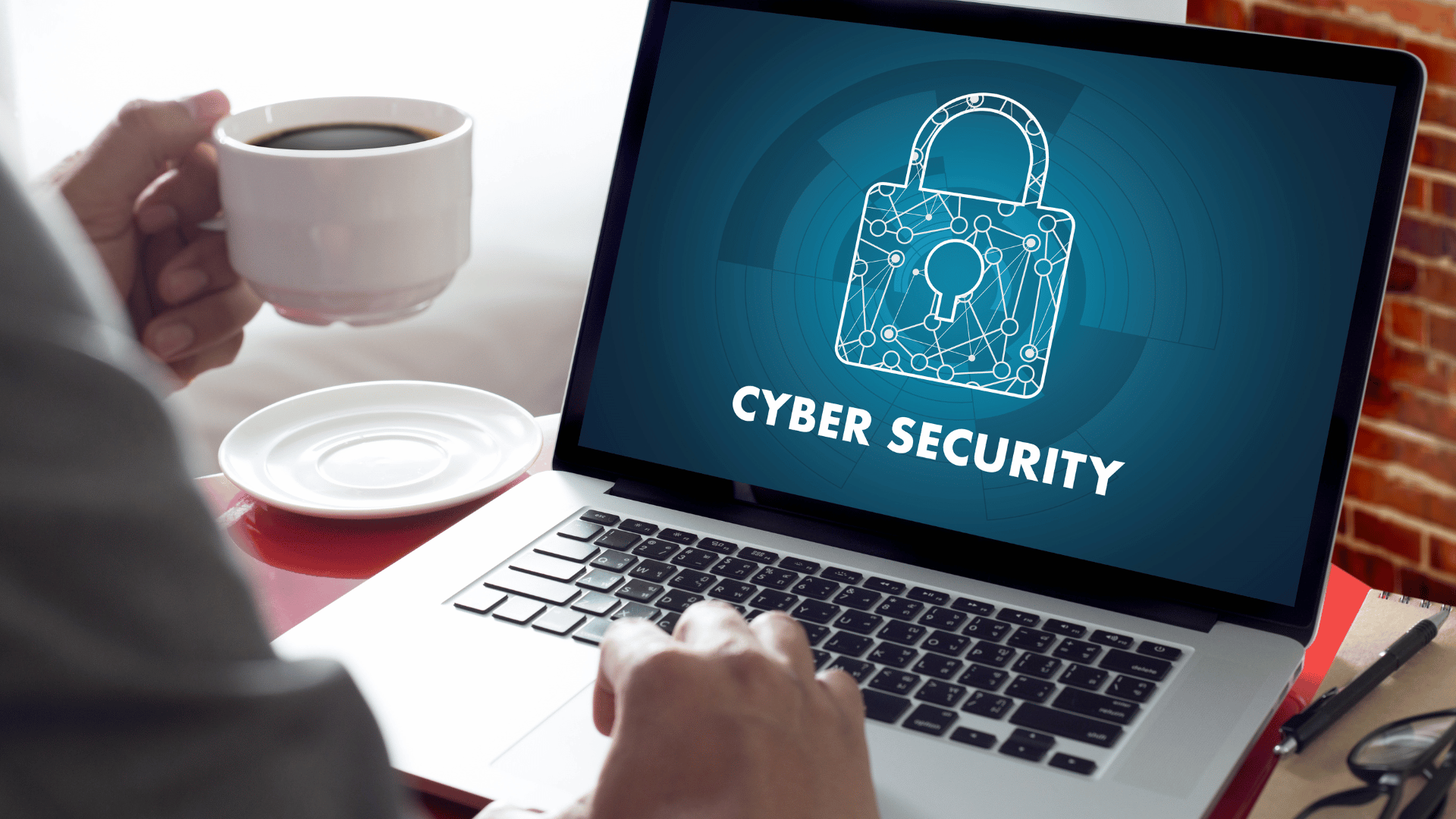 A person working through cybersecurity training on their laptop with a cup of hot coffee or tea in their left hand.