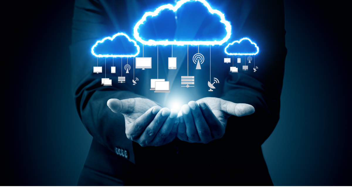 Man in a suit with hands outstretched with a holographic visual of various business icons hanging from cloud computing symbols.