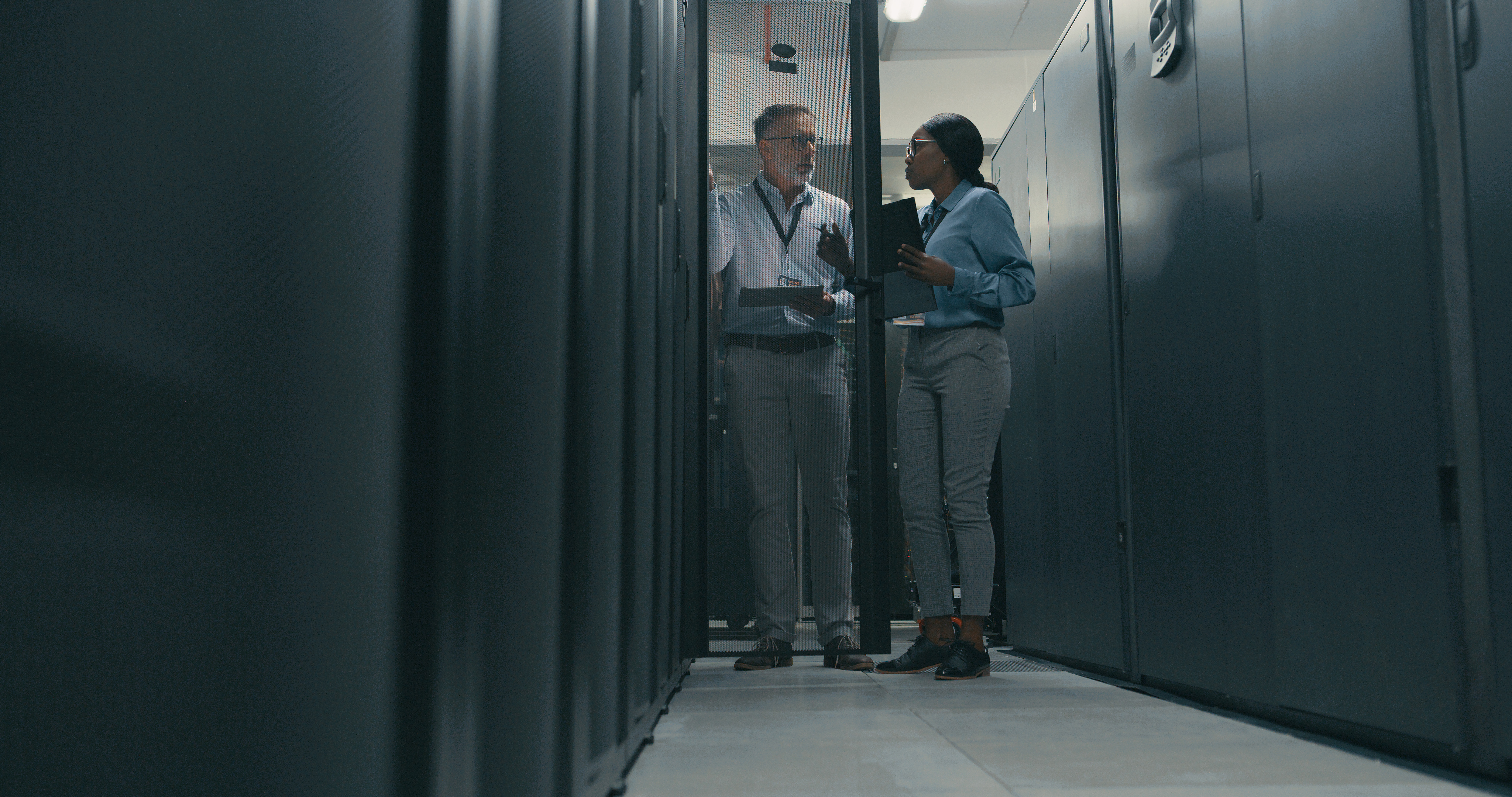 Image of two colleagues, man and a woman, standing in a corridor, seemingly in a discussion. 