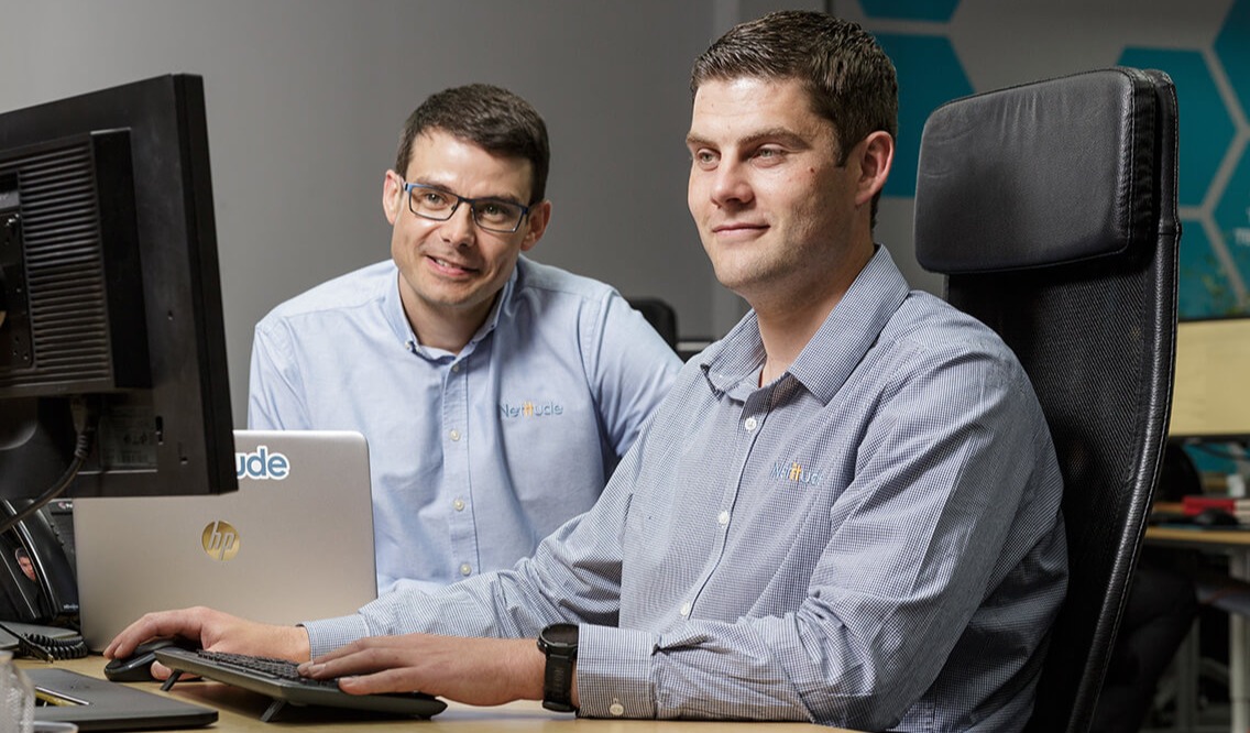 Two male IT engineers looking at a computer screen while smiling